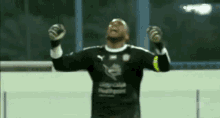 a soccer goalie is raising his arms in the air while wearing gloves .