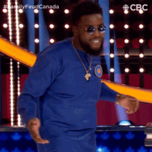a man wearing sunglasses and a blue shirt is dancing on a stage with a cbs logo in the background