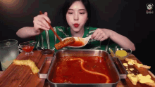 a woman in a green shirt is eating a bowl of soup