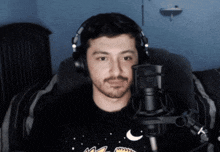 a man wearing headphones sits in front of a microphone and looks at the camera