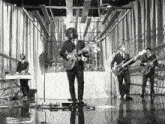 a black and white photo of a band playing guitars and singing into microphones