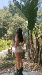 a woman in a bikini and shorts is standing in a garden