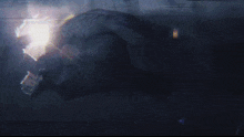 a man in a black suit is fighting another man in a dark room with a glowing light in the background .