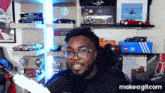 a man wearing glasses and a black shirt is sitting in front of a shelf full of toy cars