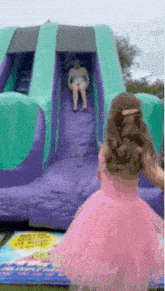 a little girl in a pink dress is standing next to a bouncy house .