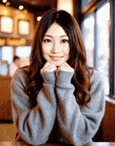 a woman in a grey sweater sits at a table with her hands folded