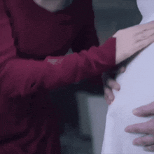 a woman in a red sweater is holding a child 's hand on her stomach .