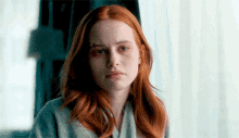 a woman with red hair is looking at the camera with a scar on her face .