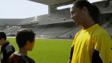 a man in a yellow shirt is talking to a young boy in a soccer field .