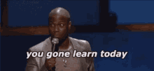 a man in a suit is speaking into a microphone and says you gone learn today .