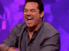 a man is laughing and pointing at the camera while standing in front of a purple background .