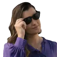 a woman wearing sunglasses and a purple shirt adjusts her sunglasses
