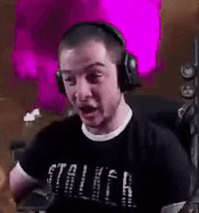 a man wearing headphones and a black shirt is sitting in front of a microphone .