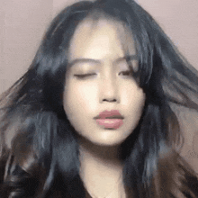 a woman with long black hair is looking at the camera with her eyes closed and her hair blowing in the wind .