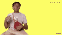 a young man is sitting on a yellow background holding a red supreme bag .
