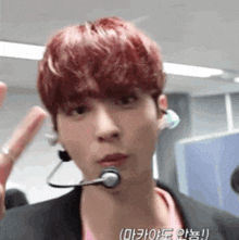 a young man with red hair is wearing a microphone and a pink shirt .