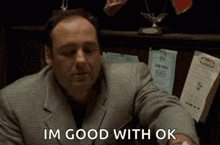 a man in a suit is sitting at a table and saying i 'm good with ok