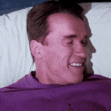 a man in a purple shirt is smiling while laying on a bed