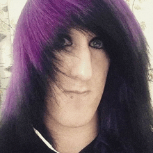 a young man with long black and purple hair is making a funny face .