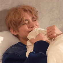 a young man is laying in bed with his eyes closed and holding a napkin to his mouth .