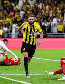 a soccer player wearing a yellow and black jersey with roshn written on it