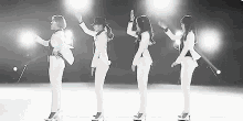 a group of women in white suits are dancing on a stage in front of a microphone .