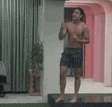a shirtless man in striped shorts stands in a room with pink walls
