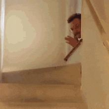 a man in a suit and tie is peeking out from behind a railing on a set of stairs .