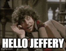 a man with curly hair is sitting on a couch and says hello jeffery .