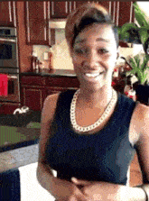 a woman wearing a black tank top and a gold chain necklace smiles in a kitchen