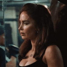 a woman in a black tank top with a necklace is standing in front of a glass wall .