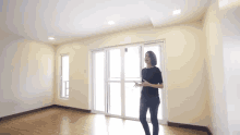 a woman is standing in an empty room with a sliding glass door and talking on a cell phone .