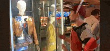 a man in a red hat is standing in front of a glass case with a mannequin .