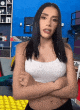 a woman in a white tank top is standing with her arms crossed in front of a blue wall .