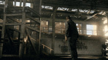 a man in a black jacket stands in an empty building with a few boxes on the wall
