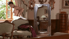 a man without a shirt is standing in front of a mirror in a living room