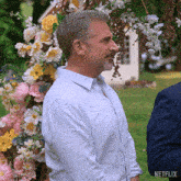 a man in a blue shirt is standing in front of a floral arch with netflix written on the bottom