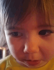 a close up of a baby 's face with a yellow shirt
