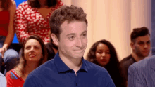 a man in a blue shirt is smiling while sitting in a crowd of people .