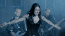 a woman in a black dress with her arms outstretched in front of a band