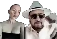 a man in a white hat and sunglasses stands next to a woman in a black top