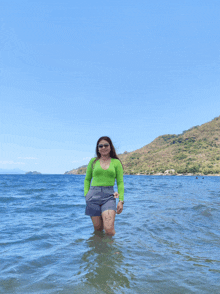 a woman in a green top and grey shorts stands in the water