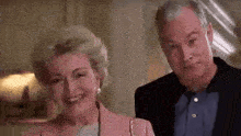 a man and a woman are standing next to each other and smiling . the woman is wearing a pink jacket .
