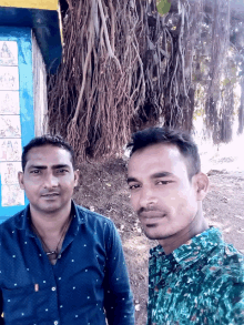 two men pose for a picture in front of a tree with roots