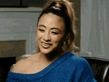 a woman wearing a blue sweater and earrings smiles