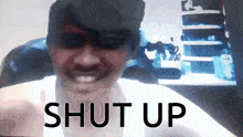 a man with a mustache is smiling in front of a screen that says " shut up "