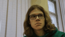 a young man wearing glasses and a green hoodie is looking at the camera