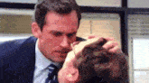 a man in a suit and tie is touching another man 's head .