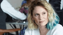 a woman with blue hair and blonde hair is sitting at a table .