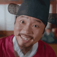 a man with a beard and mustache wearing a hat and a red shirt is smiling .